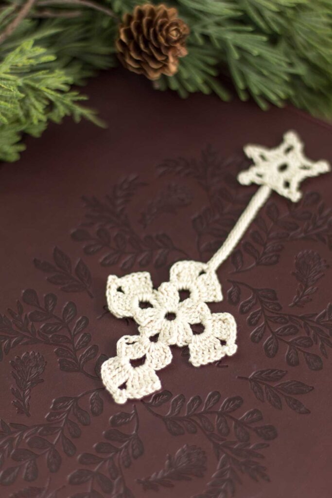 closeup of an antique white crochet thread cross bookmark with a Christmas star at the top lying on a dark brown leather bible with cedar greenery and a small pine cone next to it
