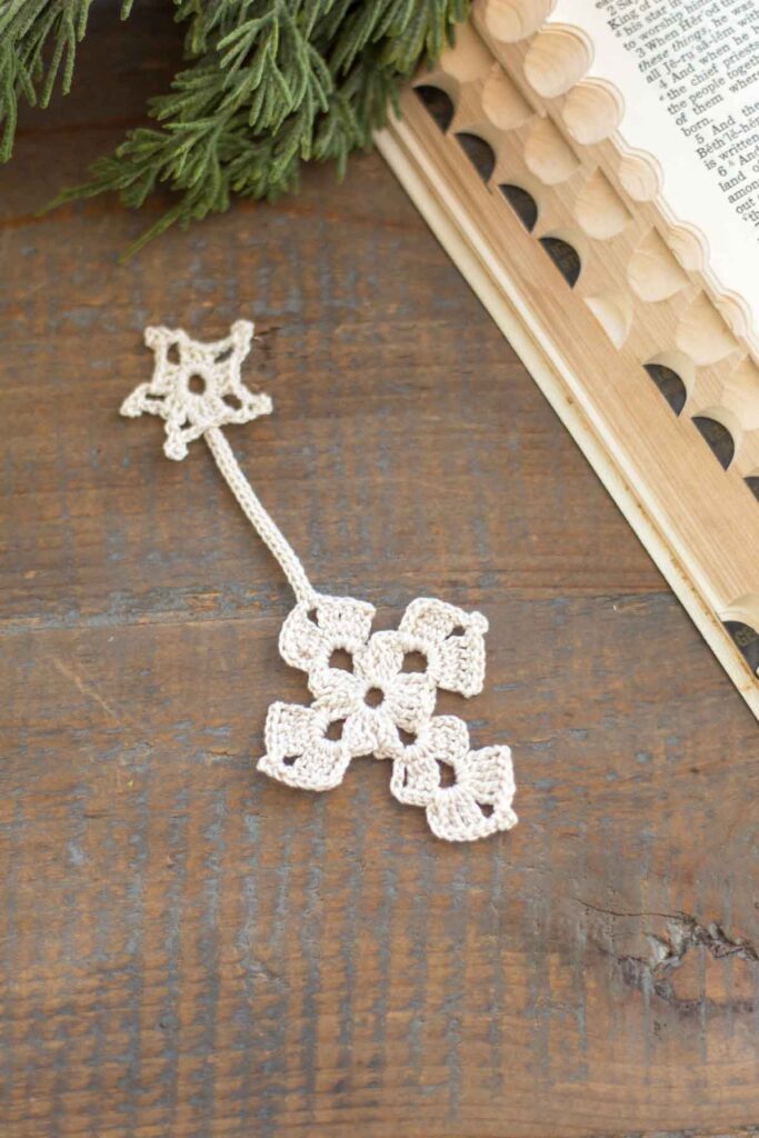 antique white crochet Christmas star and cross bookmark on a reclaimed wood farmhouse table next to an heirloom bible and cedar greenery