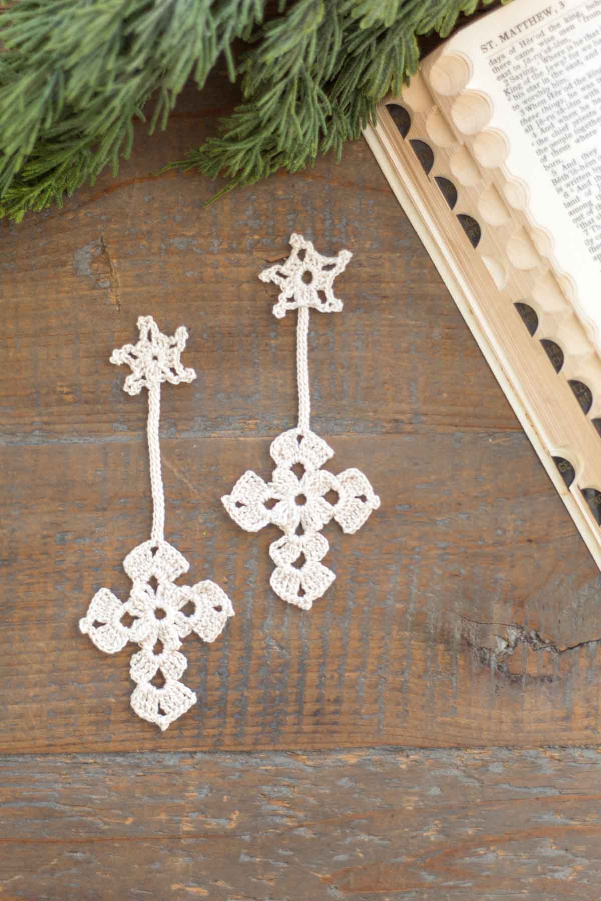two antique white crochet Christmas star and cross bookmarks on a reclaimed wood farmhouse table next to a vintage bible and cedar greenery