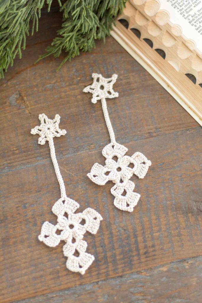 two antique white crochet Christmas star and cross bookmarks on a reclaimed wood farmhouse table next to a vintage bible and cedar greenery