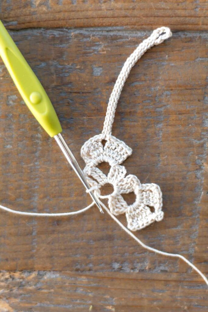 completed upper body of the cross bookmark with two rows of triple crochet stitches, chain stitches, and slip stitches in addition to the 25 stitch long chain with loop at top for the crochet star to attach to later