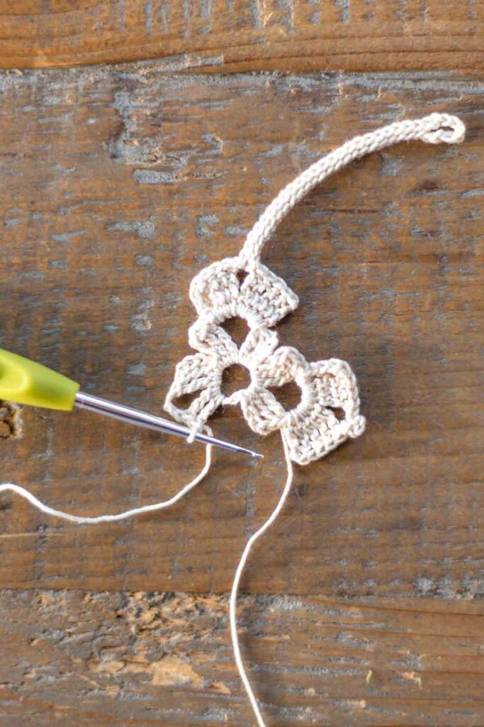 beginning of left arm of the cross bookmark with a total of 5 triple crochet stitches and 3 chain stitches in white crochet thread with hook at end of the row