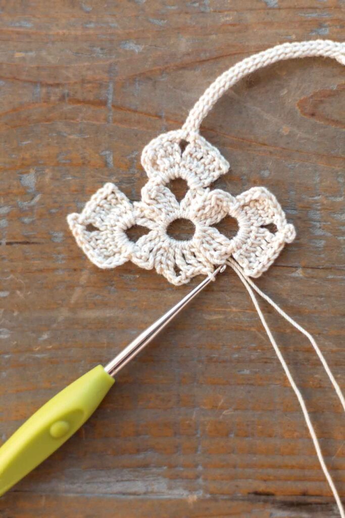 beginning of lower body of the cross bookmark with a total of 5 triple crochet stitches and 3 chain stitches in white crochet thread with hook at end of the row