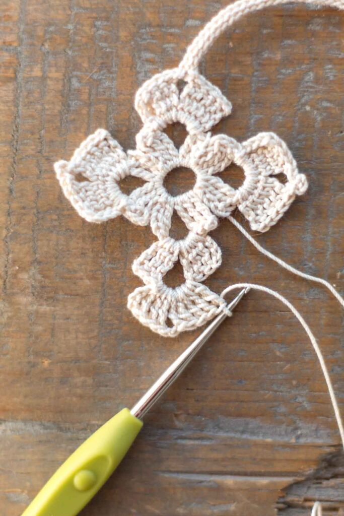 row 3 of lower body of the cross bookmark with a total of 9 triple crochet stitches and 2 chain stitches in white crochet thread with hook at end of the row